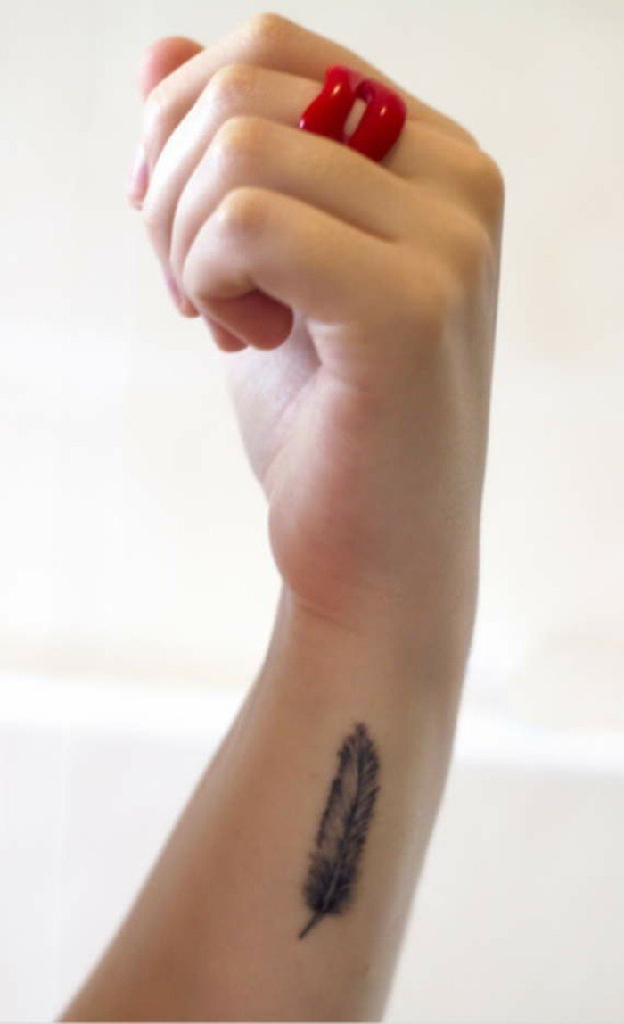 Idea tatuaggi belli, tattoo piuma sul polso della mano, anello rosso sul dito medio