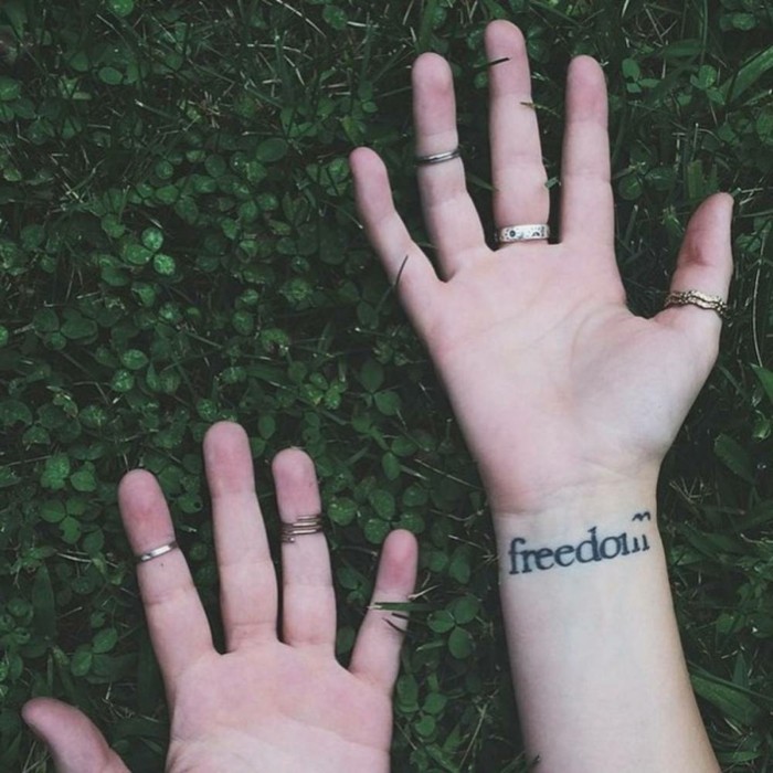 Tatuaggio con scritta sul polso, tattoo freedom in inglese, mani ragazza con anelli