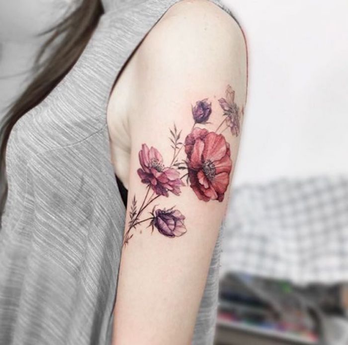 Il braccio di una donna tatuato, tattoo fiori colorati, abbigliamento con maglietta grigia