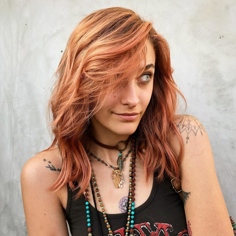 Donna con tatuaggi, colore capelli rosso, taglio scalato long bob, taglio medio mosso