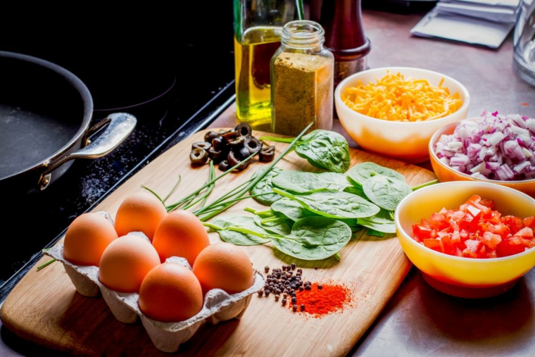 Foto di un tagliere con ingredienti, foglie di spinaci, ciotole con pomodori e cipolla, esempio dieta chetogenica