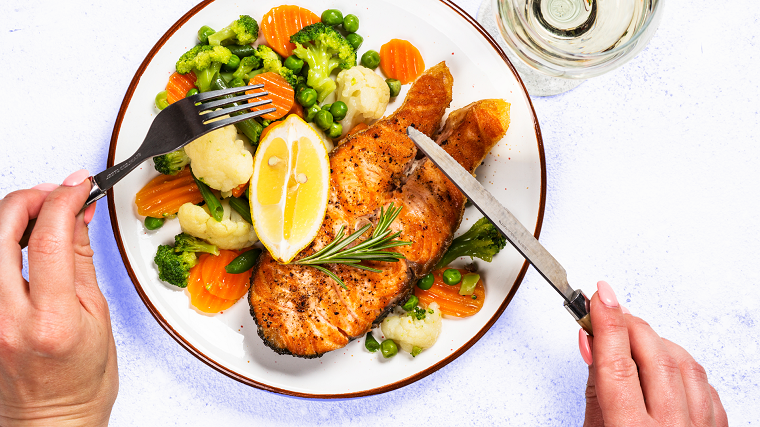 Donna che mangia, piatto di salmone, contorno di broccoli e cavolfiore, carote tagliate a fette