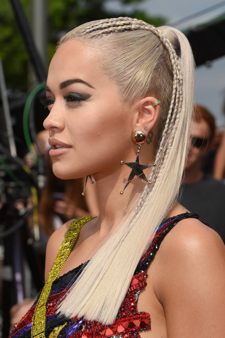 La cantante Rita Ora, capelli biondi con treccine, coda alta capelli lisci, acconciature con trecce