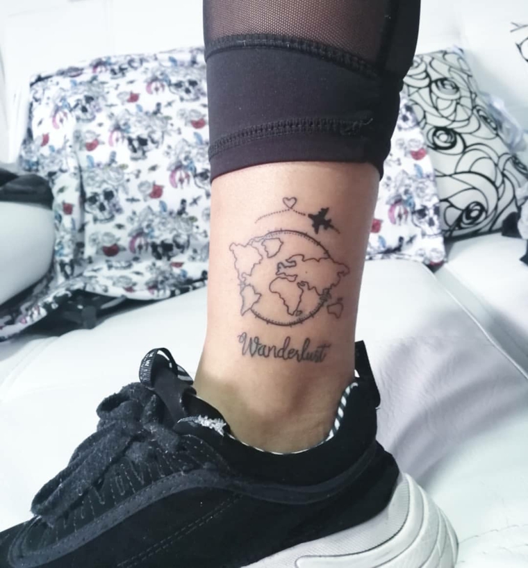 Tatuaggi colorati, tattoo sulla caviglia, scritta tattoo Wanderlust, disegno globo con continenti
