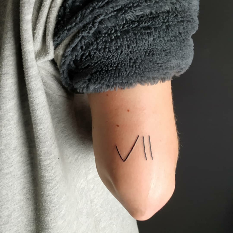 Tatuaggi piccoli particolari femminili, tattoo numero romano, donna con maglione grigio