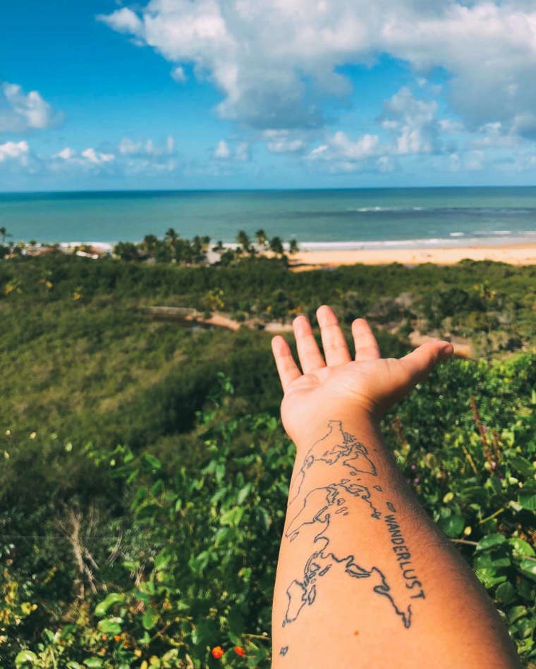 Tatuaggi fighi, tattoo sull'avambraccio, scritta Wanderlust, vista mare e spiaggia