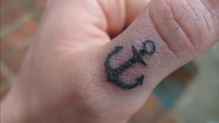 Tatuaggi significati profondi, tattoo ancora sul dito, mano di un uomo tatuata