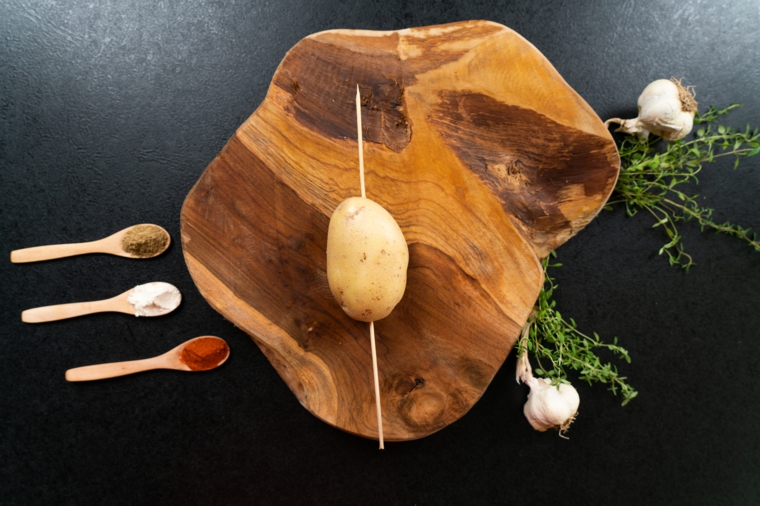 Patate a ventaglio, patata con la buccia su uno spiedino di legno, cucchiai di legno con spezie