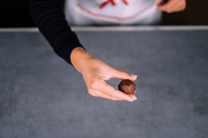 Energy ball ricetta, pallina di cacao, mano di una donna, piano di lavoro grigio, pallina energetica