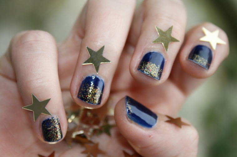 Nails natalizie, smalto colore blu, smalto oro glitter, stelline di carta, mano di una donna