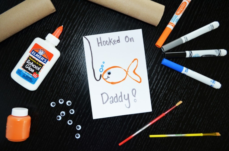 Cartolina per la festa del papà con disegno di un pesce, pennarelli colorati e tubo di colla