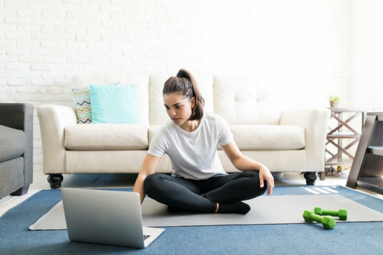 Donna sul tappetino con computer e manubri, scheda allenamento per aumentare massa muscolare a casa