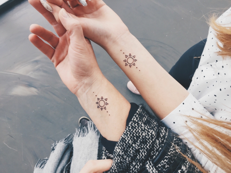 Tatuaggio simbolo amicizia, tattoo sul polso della mano di due ragazze, disegno tattoo sole