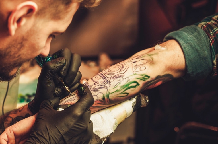 uomo con guanti che fa un tattoo idee tatuaggi uomo braccio colorati