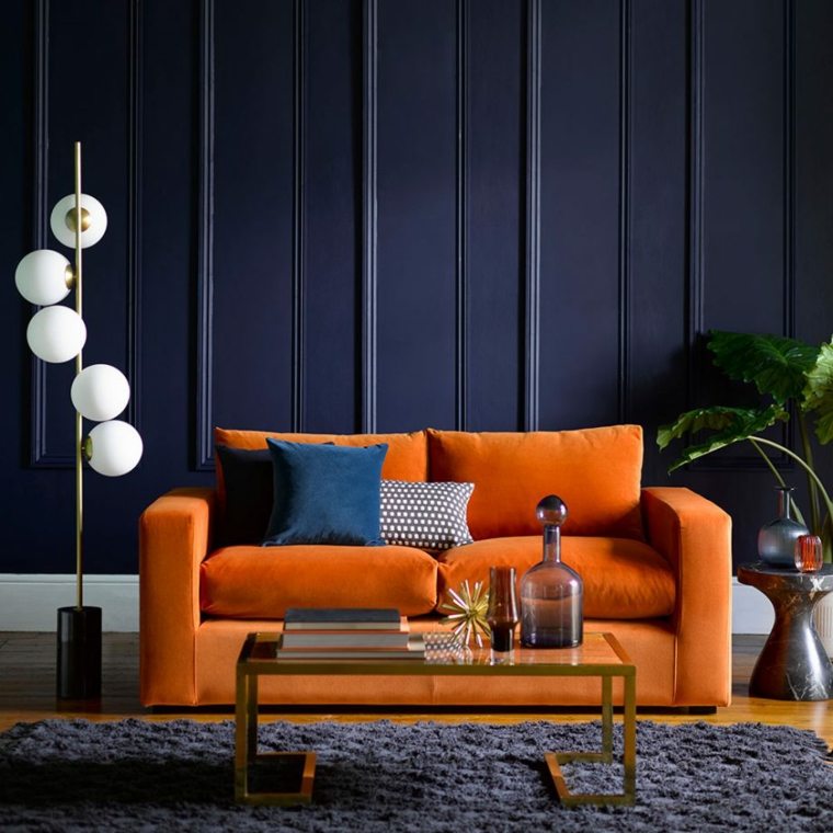divano due posti di colore arancione pannelli boiserie in poliuretano tavolino in vetro con decorazioni