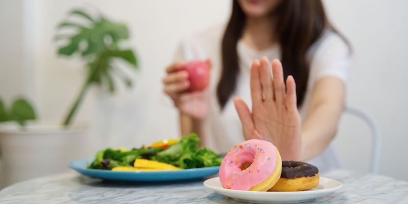young girl on dieting for good health concept. close up female using hand reject junk food by pushing out her favorite donuts and choose red apple and salad for good health.