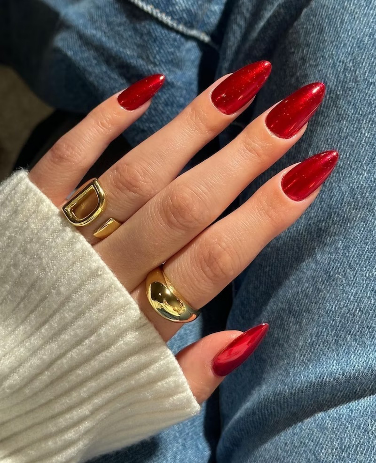 stiletto con smalto rosso glitterato mani donna con anelli in oro
